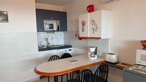 A compact kitchen with a microwave, coffee maker, and toaster on the counter, a small dining table with chairs, and a cabinet with floral decorations. - Banyuls-sur-Mer T2 with terrace and WIFI (Banyuls-sur-Mer)