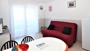 A compact living space with a dining table, red sofa, and a small kitchen area. - Banyuls-sur-Mer T2 with terrace and WIFI (Banyuls-sur-Mer)