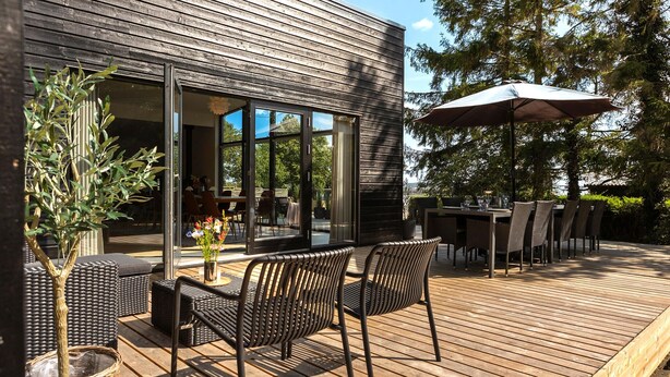 Una terraza exterior con mobiliario de mimbre, una mesa de comedor y una sombrilla.