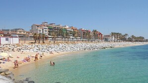 Une plage à l’eau turquoise et limpide, un rivage rocheux et des bâtiments visibles au loin.