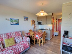 Uma sala de estar aconchegante com um sofá, uma mesa de jantar com cadeiras, uma cozinha com micro-ondas e uma cafeteira.