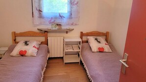 A bedroom with two single beds, a window with a floral curtain, a small table, and a radiator. - Cozy 4-person apt in Chaillol with balcony, near station (Saint-Michel-de-Chaillol)