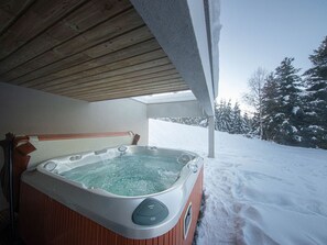 A hot tub under a wooden roof with a snowy landscape in the background.