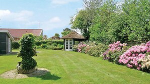 A well-maintained garden with a thatched-roof gazebo, a neatly trimmed hedge, and flowering shrubs.