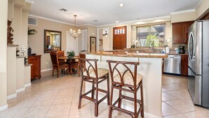 A spacious kitchen with a central island, bar stools, a dining area, and a large refrigerator.