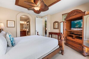 A bedroom with a large bed, a wooden dresser, a television, and a ceiling fan.