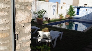 A courtyard with a pool, white lounge chairs, potted plants, and a stone wall. - Maison de Vacances a la Campagne Avec Piscine (ESSAOUIRA)