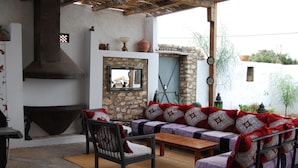 A cozy outdoor seating area with a stone wall, a fireplace, and a wooden table. - Maison de Vacances a la Campagne Avec Piscine (ESSAOUIRA)