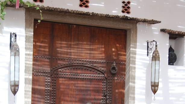 A large wooden door with metal reinforcements, flanked by two wall-mounted lanterns. - Maison de Vacances a la Campagne Avec Piscine (ESSAOUIRA)