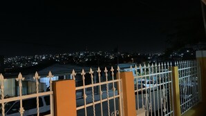 A night view from a balcony with a metal railing, overlooking a cityscape with illuminated buildings. - Cozy 3 bedroom house in Ensenada Mexico (Ensenada)