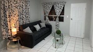A living room with a black sofa, patterned curtains, a glass coffee table, and a white door. - Cozy 3 bedroom house in Ensenada Mexico (Ensenada)