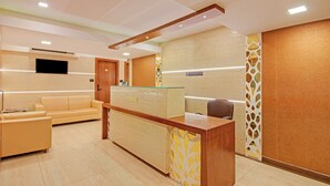 A reception area with a wooden reception desk, a sofa, a TV mounted on the wall, and a reception sign. - Treebo Trend Oxford (Mumbai)