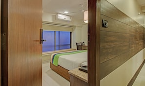Ein Hotelzimmer mit einem Bett, einem Nachttisch mit Telefon, einem Fenster mit Jalousien, einem Deckenventilator und einer Klimaanlage.