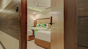 A hotel room with a wooden wall panel, a bed with a headboard, a nightstand, and a ceiling fan. - Treebo Trend Oxford (Mumbai)