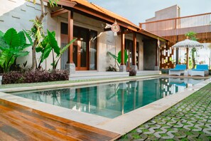 A pool area with a wooden deck, a stone pathway, and a covered seating area with umbrellas. - The Ume Cemagi (Cemagi)
