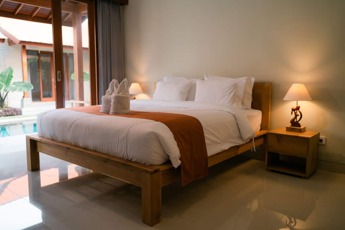A large bed with a wooden frame, white bedding, and a brown throw blanket. There are two bedside tables with lamps.