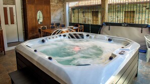 A hot tub in a room with stone walls, a wooden door, and a dining area with chairs. - FIFTH DO SOUTO (Barcia de Mera - COVELO)