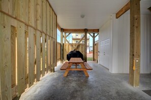 Ett takförsett utomhusområde med ett picknickbord och en grill, omgivet av träväggar och ett betonggolv.