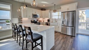A modern kitchen with white cabinets, stainless steel appliances, and a large island with bar stools. - Experience coastal views at Topsail Turvy, a spacious 4-bedroom home in North Topsail Beach. (North Topsail Beach)