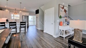 A modern kitchen with white cabinets, a dining area with wooden chairs, and a staircase leading to a balcony. - Experience coastal views at Topsail Turvy, a spacious 4-bedroom home in North Topsail Beach. (North Topsail Beach)