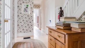 A hallway with floral wallpaper, a wooden dresser with books, and a staircase. - 12 Hurst - Chautauqua Charmer (Chautauqua)