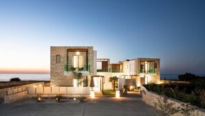 Een modern huis met twee verdiepingen, een stenen gevel, grote ramen en een balkon met uitzicht op zee.