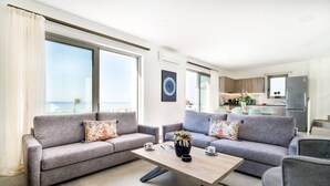 Een moderne woonkamer met twee grijze banken, een salontafel en uitzicht op zee door grote ramen.