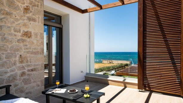Een balkon met een stenen muur, een tafel met drankjes en uitzicht op zee.