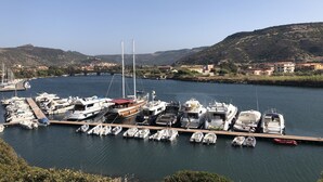 A marina with various boats docked, a bridge in the background, and a hilly landscape. - Figoli guesthouse (Oristano)