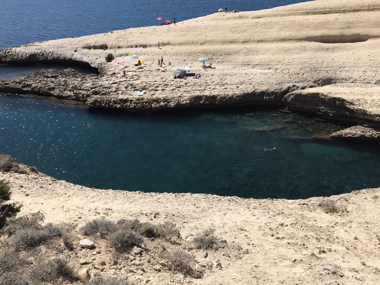 Ein felsiger Strand mit klarem, blauem Wasser, einigen Personen und ein paar Sonnenschirmen.