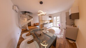 A modern kitchen with a central island, a spiral staircase, and a dining area with glass-top tables. - Figoli guesthouse (Oristano)