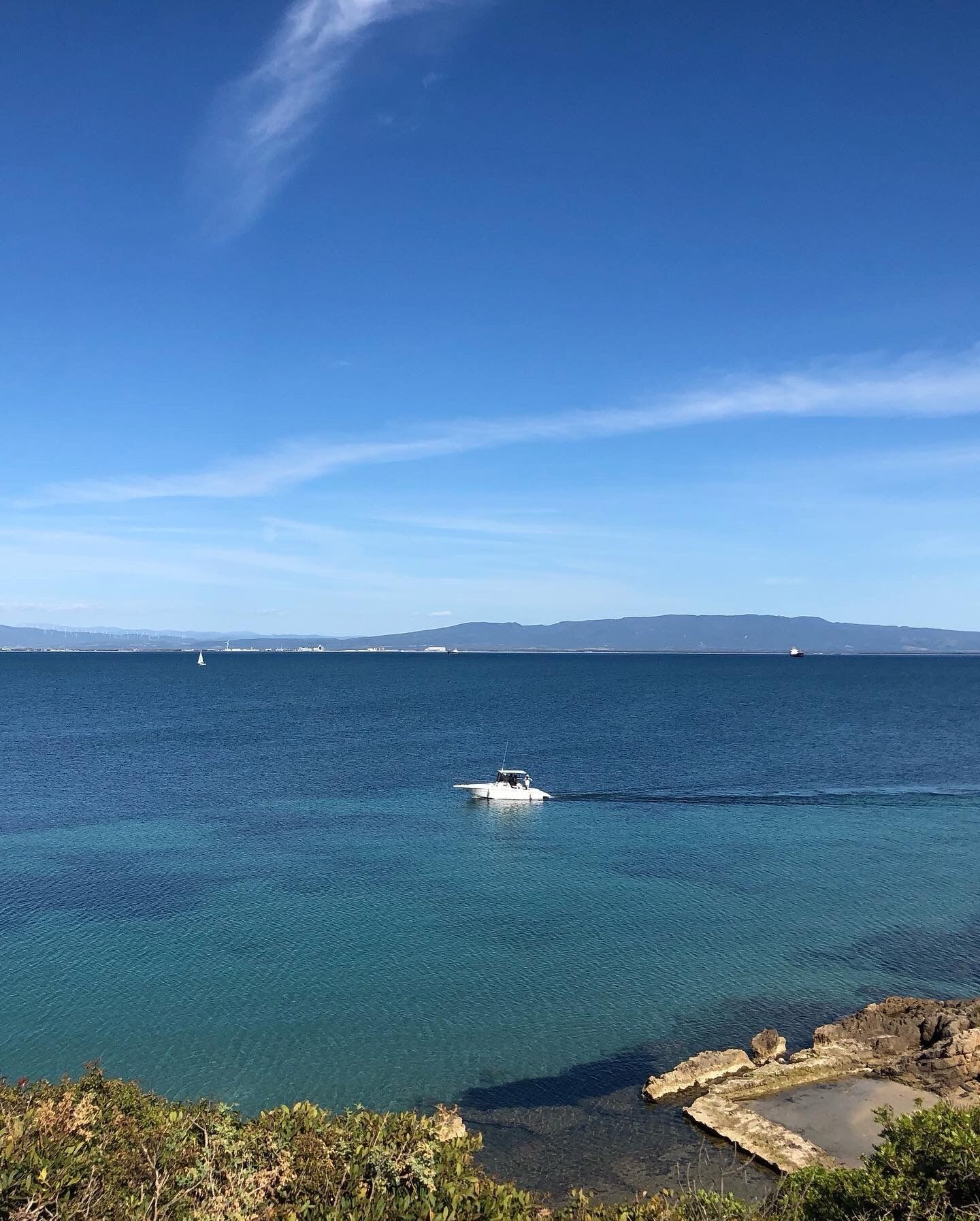 Une vue sur la côte, avec un bateau sur l’eau, un ciel dégagé et des montagnes à l’horizon.