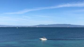 Une vue sur la côte, avec un bateau sur l’eau, un ciel dégagé et des montagnes à l’horizon.