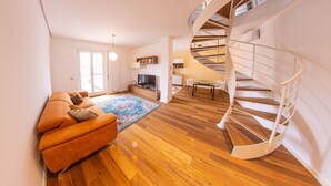 A modern living room with a spiral staircase, wooden flooring, a sofa, and a TV. - Figoli guesthouse (Oristano)
