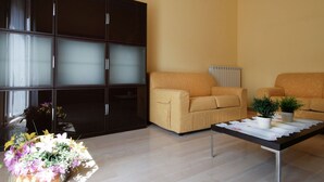Een moderne woonkamer met een grote donkere kast, twee beige banken, een bijzettafeltje met decoratieve objecten en een potplant.