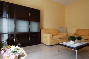 A modern living room with a large dark cabinet, two beige sofas, a coffee table with decorative items, and a potted plant.