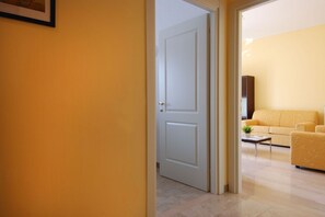 A hallway with a closed door leading to a living area with a yellow sofa and a small table.