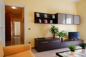 A living room with a sofa, a TV, a cabinet with shelves, and potted plants.