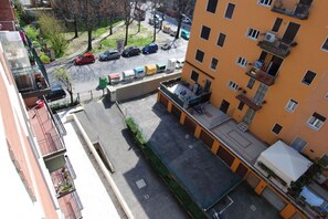 An aerial view of a multi-story residential building with balconies, a parking area, and a street with parked cars.