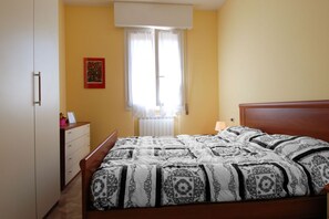 A bedroom with a bed, a dresser, a window with curtains, and a wall-mounted picture.