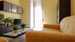 Een woonkamer met een bank, een flatscreen televisie, een salontafel met planten en een schuifpui die uitkomt op een balkon.