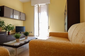 A living room with a sofa, a flat-screen TV, a coffee table with plants, and a sliding glass door leading to a balcony.