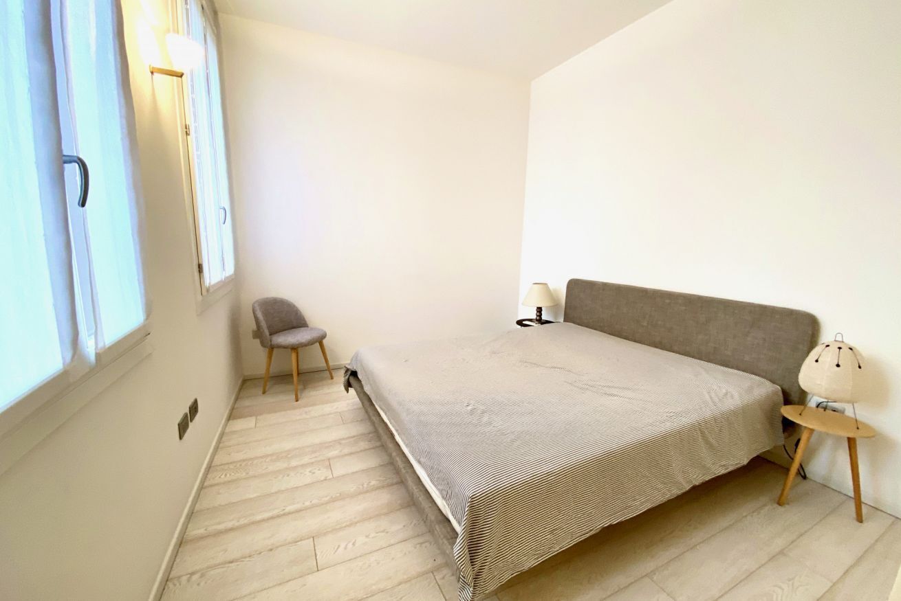 Een kleine, lichte kamer met een bed, een stoel en een lamp.