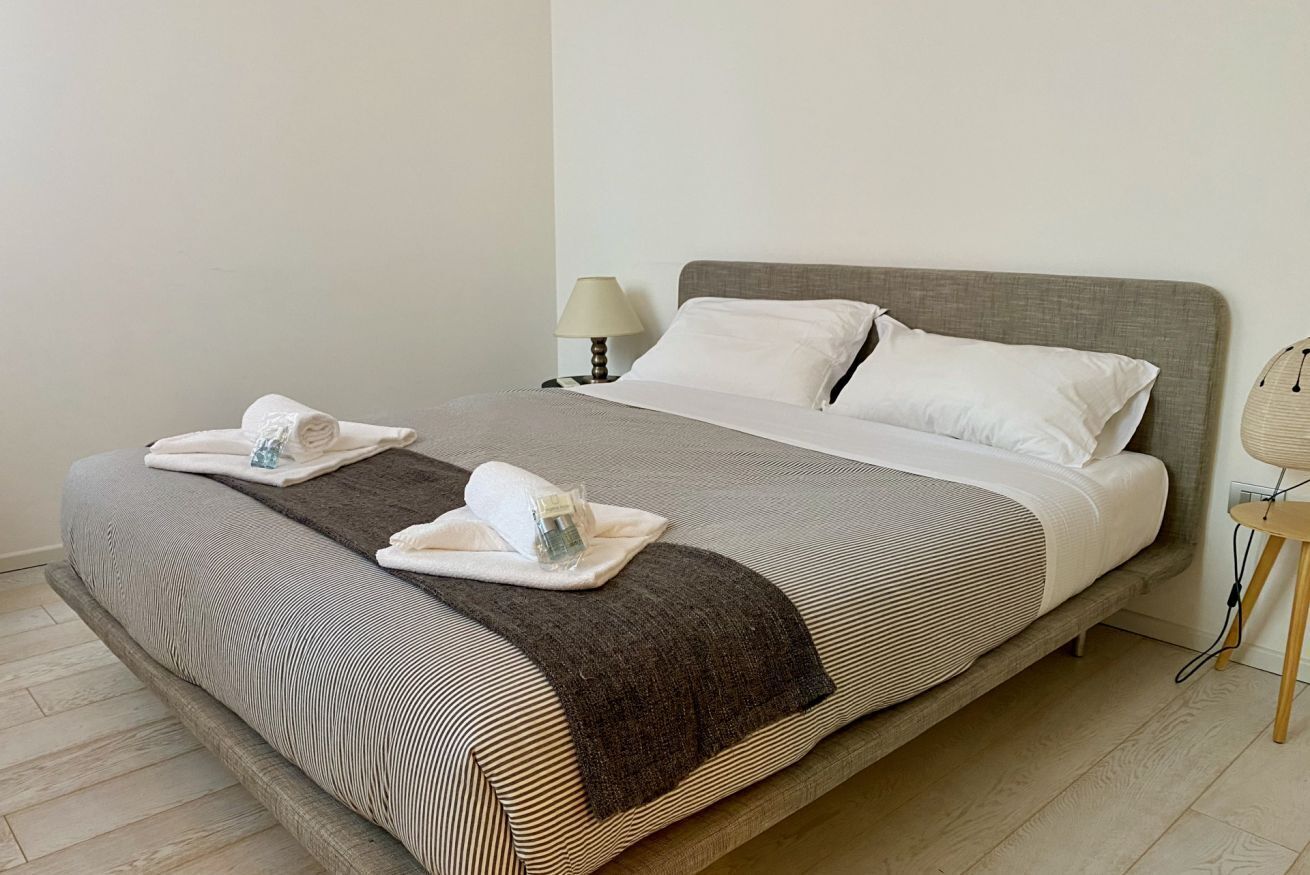 Una cama bien hecha con una colcha a rayas, dos almohadas y una toalla doblada al lado.