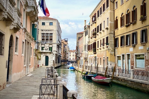 Un canal estrecho en una pintoresca ciudad europea, con edificios a ambos lados, una bandera y barcos amarrados a lo largo del agua.