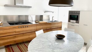 Et moderne køkken med en central ø, rustfrie hvidevarer og et rundt marmorbord.