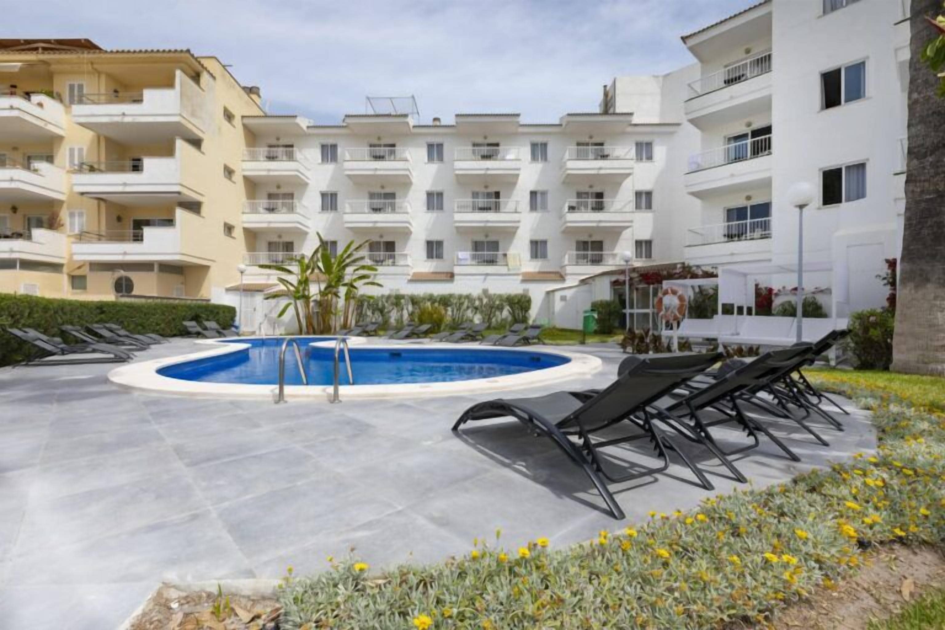 Una piscina rodeada de sillas de descanso, con un edificio al fondo.