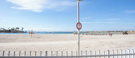 Une plage avec une clôture blanche, un lampadaire et un panneau indiquant qu’il est interdit de faire du vélo.