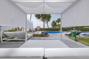 A covered outdoor area with a pool, lounge chairs, and a trash bin. - Sand Beach Apartments (Alcúdia)