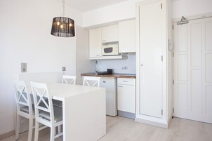 Una cocina moderna con armarios blancos, microondas, lavavajillas y una zona de comedor con mesa y sillas blancas.